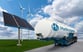 Tanker truck labeled H2 Hydrogen next to a solar panel and a wind turbine under blue skies.